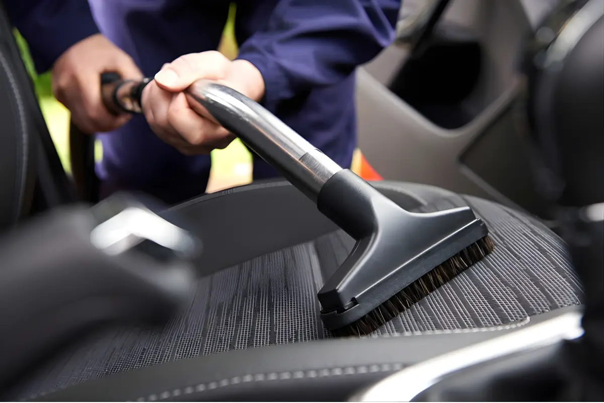 Technician vacuuming a car seat with a brush attachment during a Car Ninza interior eco-clean